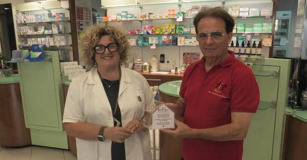 Il dott. Renzo Pili di AIL Cagliari consegna la casetta salvadanaio alla dott.ssa Maria Pia Orrù, presidente di Federfarma Cagliari, nella Farmacia Orrù.